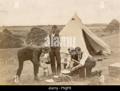 Edwardian postcard of young men camping in the countryside, cooking on an open fire outside canvas tent, circa 1905, U.K Stock Photo