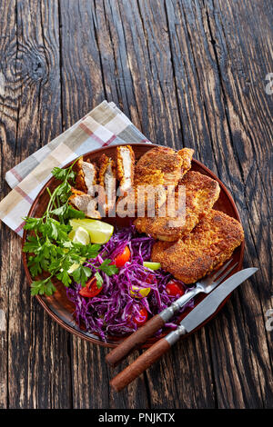 Vertical orientation of pork nuggets, breaded and spiced with lime wedges, fresh parsley and salad from red cabbage, tomatoes and pepper, served on a  Stock Photo