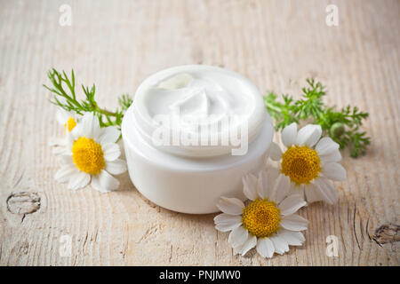 container with cream and chamomiles on wooden background Stock Photo