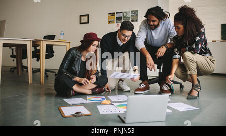 Business colleagues discussing work sitting on floor with laptop and business documents. Creative business people discussing ideas spreading their wor Stock Photo
