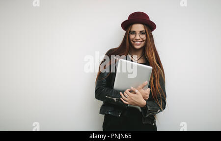 Smiling businesswoman standing against a white background holding a laptop. businesswoman wearing hat and eyeglasses holding a laptop. Stock Photo