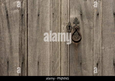 Old weathered english oak door bleached by sunshine and showing metallic stains from covered steel nails, closed with impressive knocker and keyhole Stock Photo