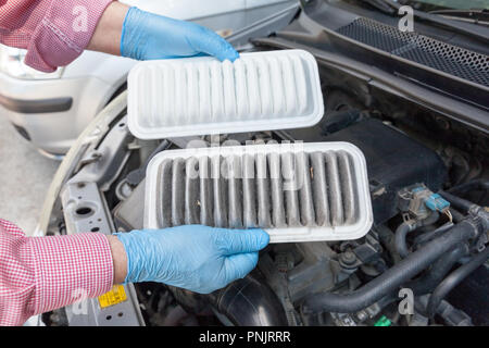 Automechanic holding dirty and clean engine air filters over a car engine. Car service and maintenance. Stock Photo