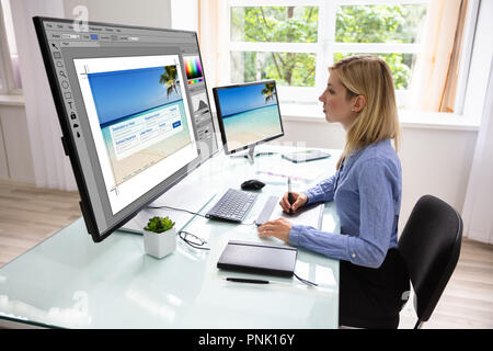 Side View Of A Young Female Designer Using Graphic Tablet While Working On Computer Stock Photo