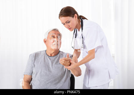 Young Female Doctor Examining Senior Male Patient's Pulse In Clinic Stock Photo