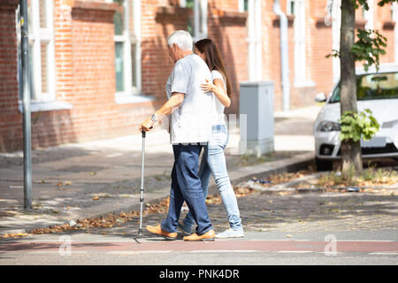 Side View Of A Young Woman Assisting Her Father While Crossing Road Stock Photo