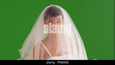 Elegant bride with veil covering face smiling at camera on green screen Stock Photo