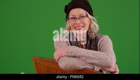 Charming old woman smiling at camera sitting on park bench on green screen Stock Photo