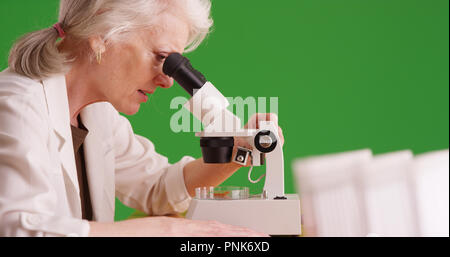 Senior scientist examining test sample with microscope in lab on green screen Stock Photo