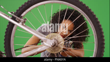 Handy black female doing repairs on her bicycle on green screen Stock Photo