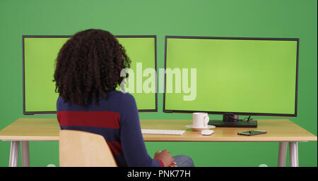 Black woman worker sitting at desk with green screen computers on green screen Stock Photo