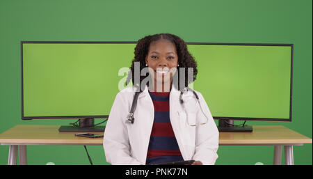 Confident black female medical professional sitting by green screen computers Stock Photo