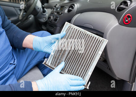 Auto mechanic,wearing protective blue gloves, showing dirty car cabin air filter. Old car cabin pollen filter replacement Stock Photo