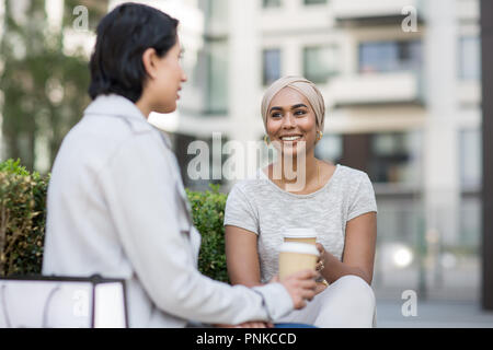 Female Muslim friends having coffee together outdoors Stock Photo