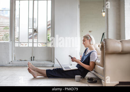Millennial using smartphone and laptop in a loft apartment Stock Photo