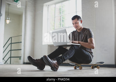 Young adult male working on laptop with skateboard Stock Photo