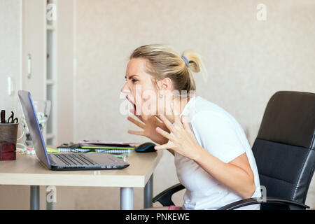angry blonde woman working on laptop at home and screaming. Freelance, work at home concept Stock Photo
