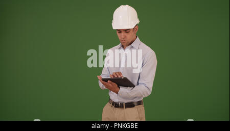 Latino architect contractor working on tablet wearing hard hat on green screen Stock Photo