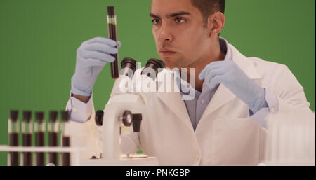 Millennial Hispanic medical scientist looking through microscope on green screen Stock Photo