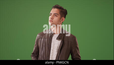 Handsome Hispanic man in leather jacket standing looking serious on green screen Stock Photo