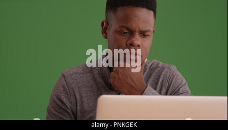 Young black man working on a laptop on green screen Stock Photo