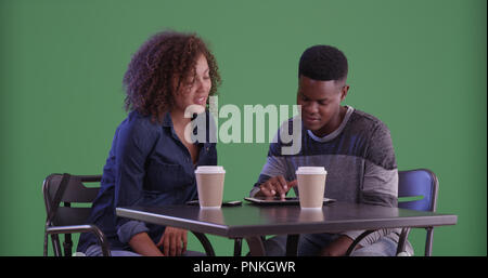 Young black man and woman having coffee using smartphone on green screen Stock Photo