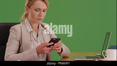 Businesswoman sitting at desk texting client on phone on green screen Stock Photo