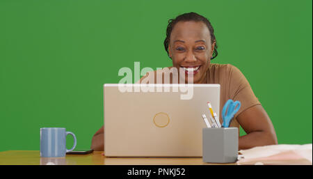 Mature black woman using laptop smiling at camera on green screen Stock Photo