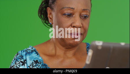 Old African-American woman using tablet device on green screen Stock Photo