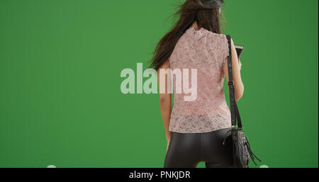 Brunette woman with back to camera using smartphone on green screen Stock Photo