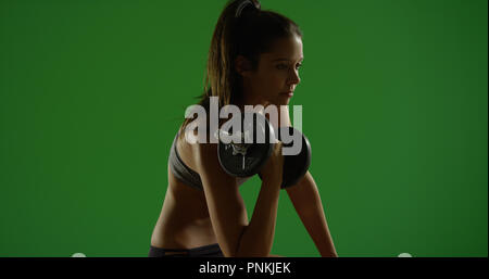 Young white woman works out while sitting down on green screen Stock Photo
