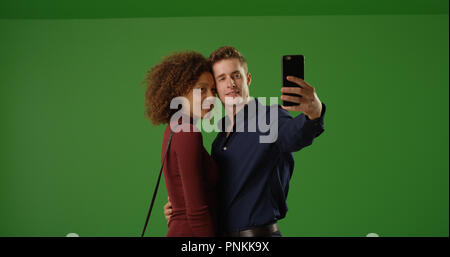 Happy interracial couple using smartphone to take selfie on green screen Stock Photo