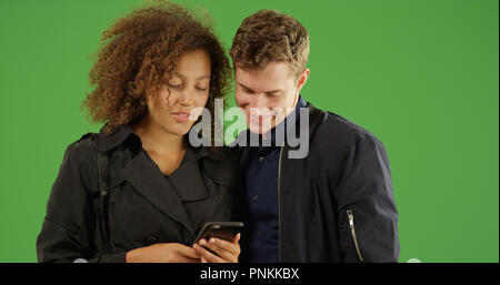 Young interracial millennial couple using phone together on green screen Stock Photo