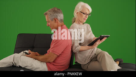Senior couple using devices on couch at home on green screen Stock Photo