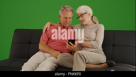 Elderly couple sitting on couch using smartphone on green screen Stock Photo