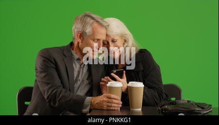 Senior woman showing her date photos on smartphone at cafe on green screen Stock Photo