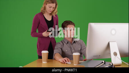 Woman using tablet standing by male coworker working on desktop on green screen Stock Photo