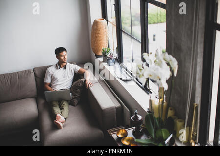 Young adult Asian male looking out of apartment window Stock Photo