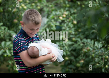 Belarus, Gomel, on July 14, 2018. A holiday in the village of Zyabrovka. Brother with a newborn sister in an apple orchard Stock Photo