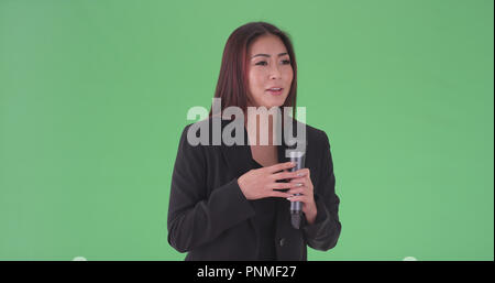 Asian millennial businesswoman speaking through microphone on green screen Stock Photo