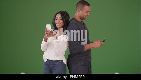 Couple standing back to back texting on cell phones on green screen Stock Photo