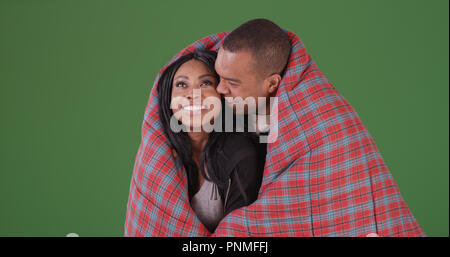 Loving black couple wrapped up in sleeping bag on green screen Stock Photo