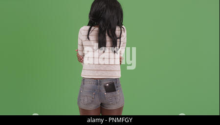 Woman with arms crossed facing away from camera on green screen Stock Photo