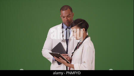 Two black doctors discuss their patient while on their tablets on green screen Stock Photo