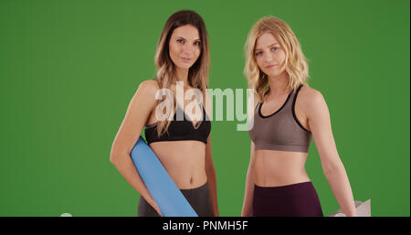 Attractive fitness girls in sportswear standing with yoga mats on green screen Stock Photo