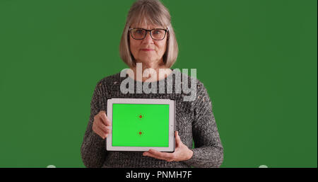 Senior woman showing tablet with green screen display to camera on green screen Stock Photo