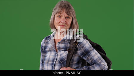 Mature stern Caucasian woman posing with backpack standing on green screen Stock Photo