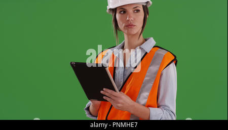 Female construction worker in orange vest and hard hat using pad on green screen Stock Photo