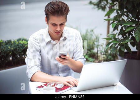 Smart attitude. Positive handsome man using a laptop and sitting in the cafe while surfing the internet. Stock Photo