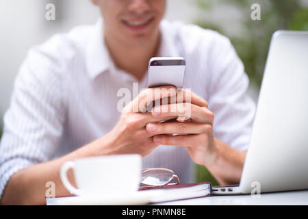 Businessman in white shirt using mobile smart phone and working or browsing internet on laptop computer. Close up photo. Stock Photo